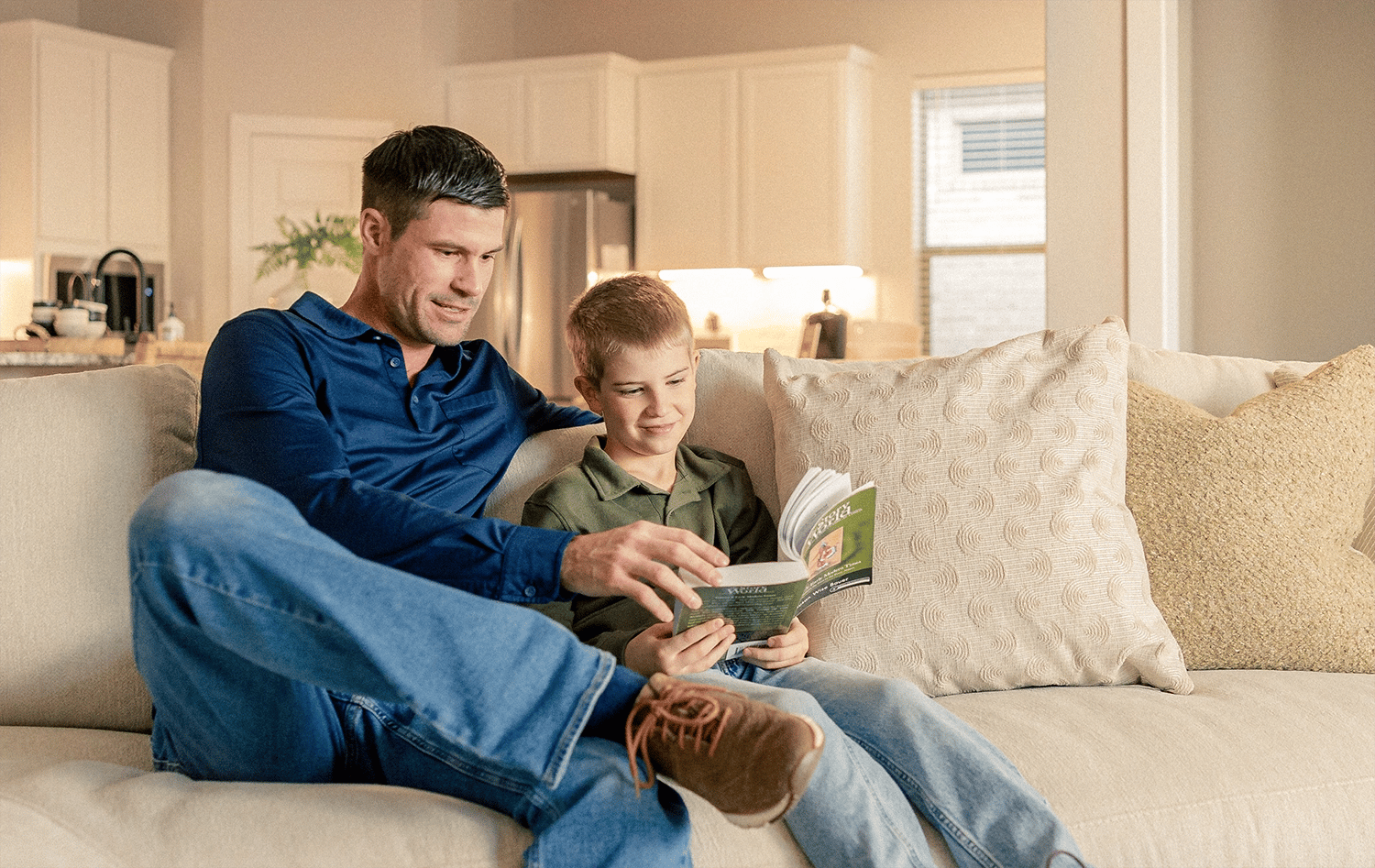 A little boy and his father reading a book together on their couch