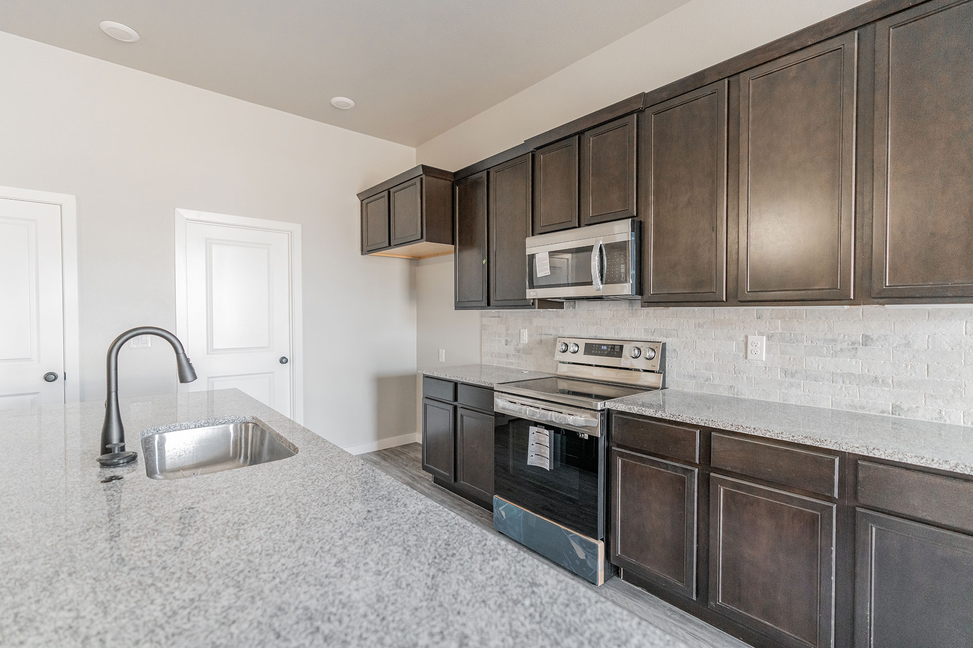 Photo of a Betenbough home kitchen with dark cabinets, granite countertops, stainless steel appliances, and a tiled backsplash.