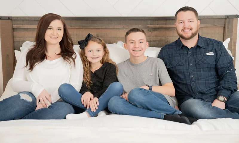 Photo of a family (mom, daughter, son, and dad) posed on a bed in their Betenbough home.