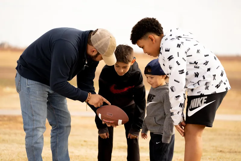 Photo of a man playing football with three boys in a Betenbough Homes community.