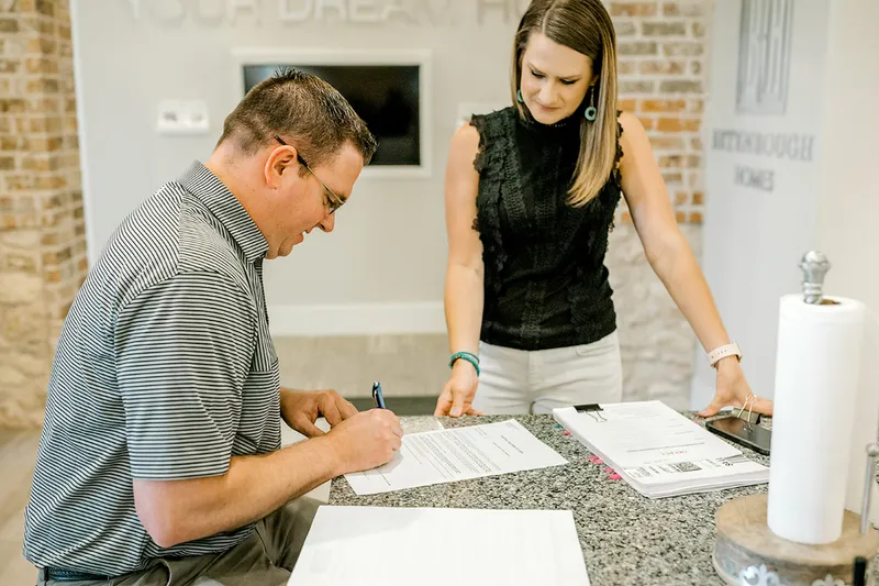 Photo of a home buyer signing documents while a Betenbough Homes team member observes.