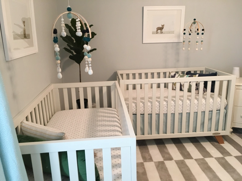 Photo of nursery decor depicting two cribs, two mobiles, and two framed images of a baby fox.