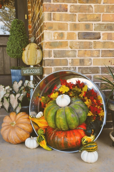 Photo of a Betenbough home front porch decorated with pumpkins, caladiums, a fall wreath, gourds, and a metal washtub.