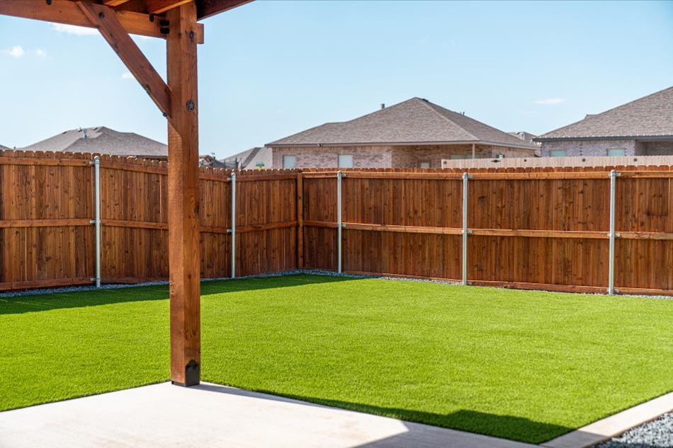 Photo of a Betenbough Home's backyard with green grass and a sturdy fence for keeping a pet safe.