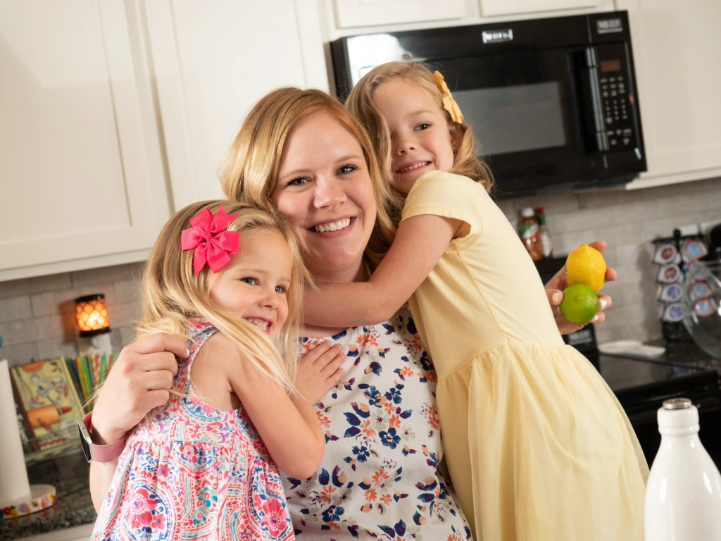 Photo of a mom with two daughters in her Betenbough cottage-style home's kitchen.