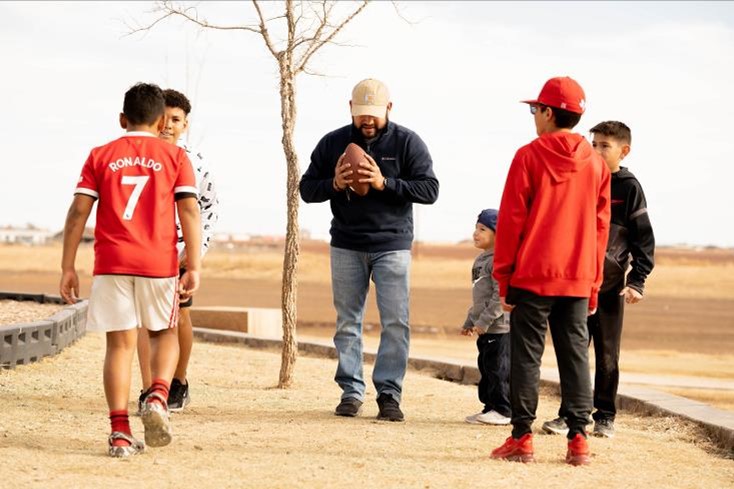 Photo of man with a football surrounded by five boys in a community park. Parks are often found in HOA communities.