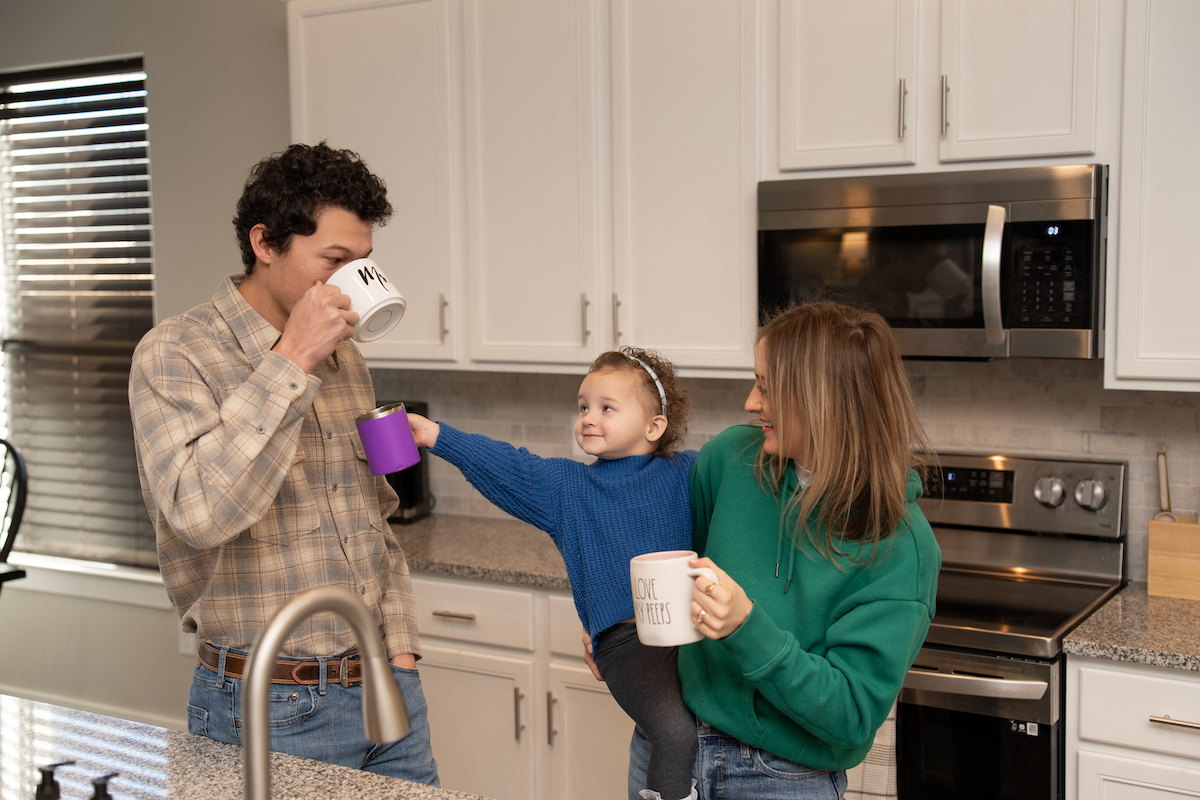 Photo of a husband and wife drinking coffee in their affordable new home. The woman is holding a child.