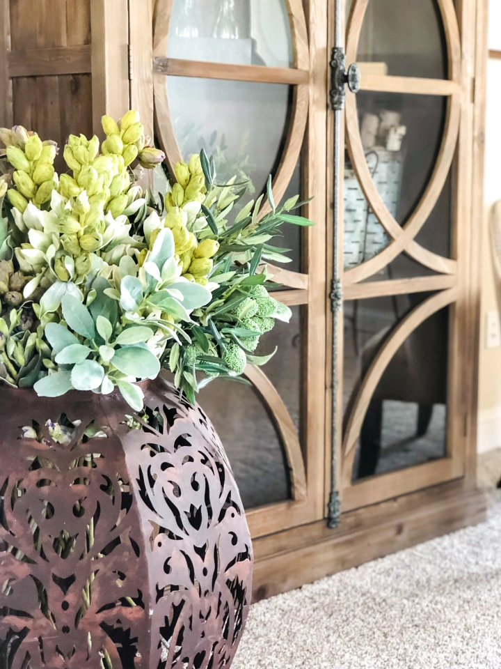 Photo of a large arrangement of greenery on the floor of a Betenbough homes living room next to a display cabinet.