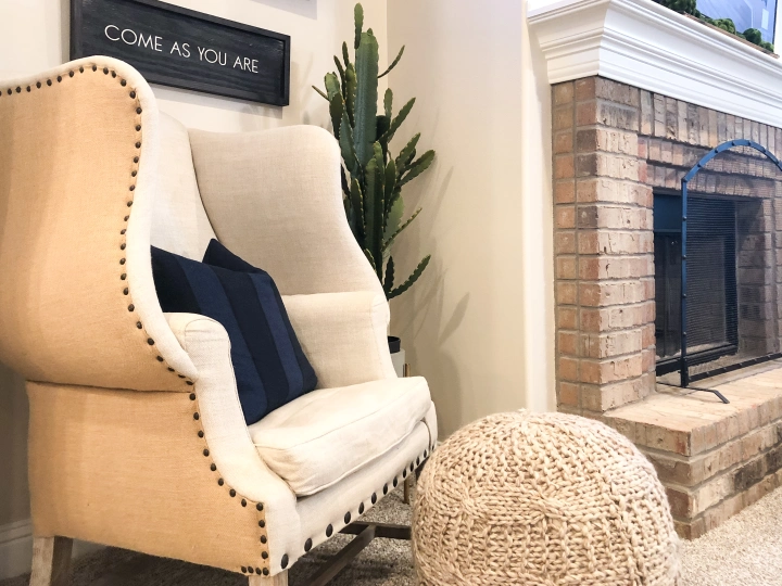 Photo of a potted cactus next to a wingback chair and cable-knit ottoman next to the fireplace in a Betenbough home.