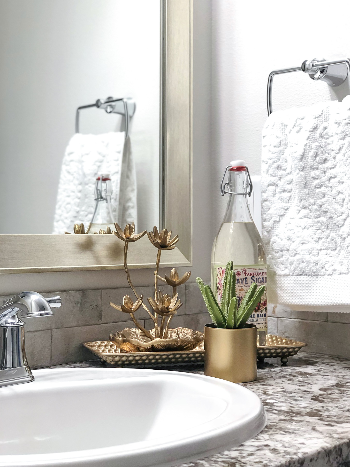 Photo of a small potted cactus arranged with a decorative bottle of soap and brass accent pieces on the granite countertop in a Betenbough homes bathroom.