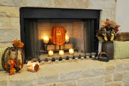 Photo of a fireplace decorated with a carved pumpkin, candles, and fall silk arrangements.